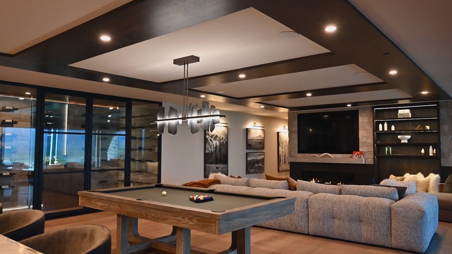 Modern entertainment room with pool table, plush sectional sofa, fireplace, built-in shelves, and sophisticated ceiling lighting