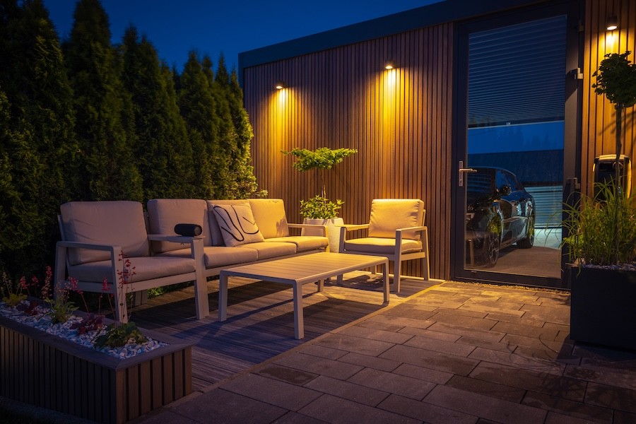 Outdoor lighting on an exterior wall illuminates patio seating at night.
