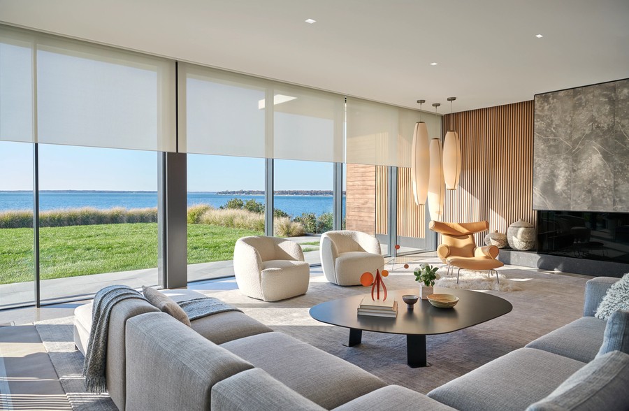A living room with Lutron shades partially lowered over a row of windows overlooking a lake.